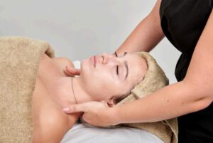 A woman lying on her back covered with a towel having lymphatic drainage therapy from a professional massage therapist.