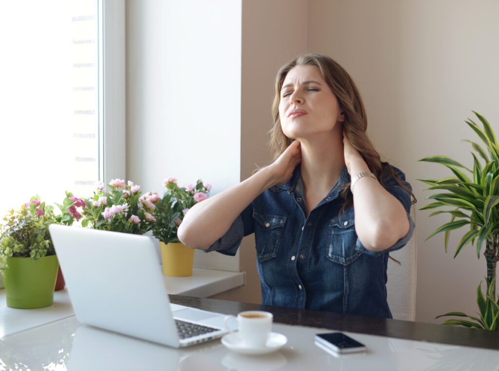 Woman experiencing neck pain after a long period of time working, using her laptop