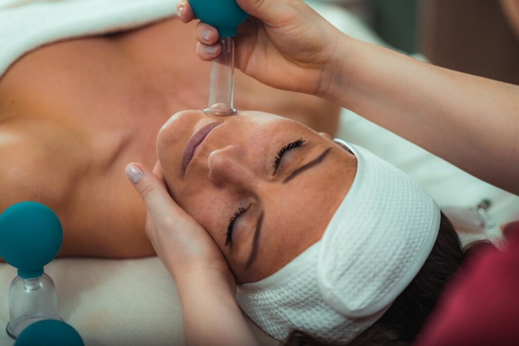 TMJ Massage Downtown Brooklyn: A woman receives facial cupping therapy while lying on a massage table, with hands gently supporting the face to relieve tension and improve circulation.