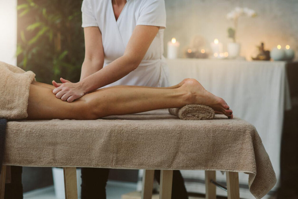Sports Massage for Injury Prevention: A massage therapist in a white uniform performs a leg massage on a client in a serene spa setting featuring soft lighting and candles.