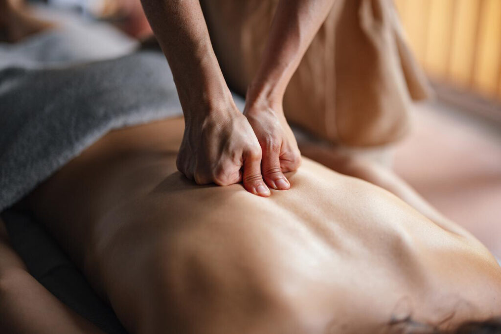 Sports Massage for Injury Prevention: A massage therapist applies deep pressure to a client's back using their knuckles and thumbs during a spa treatment.