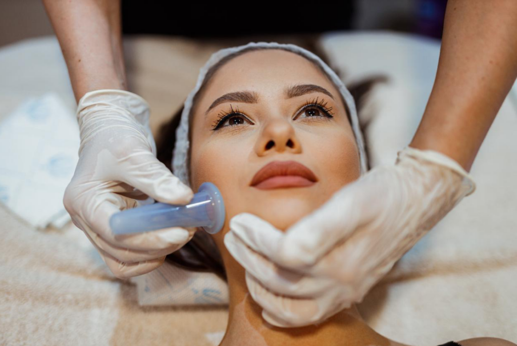 Beauty therapist’s surgically gloved hands performing facial cupping on a beautiful young woman.